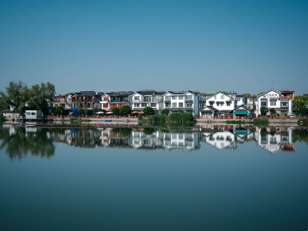 Charming traditional homes reflecting in calm lake waters under a clear blue sky.